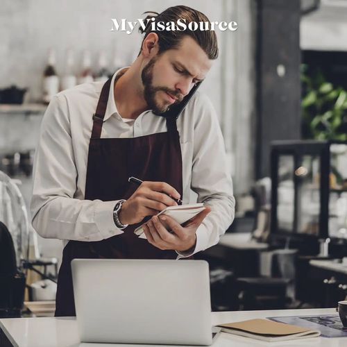 a young man at a business on his cell and taking notes by my visa source